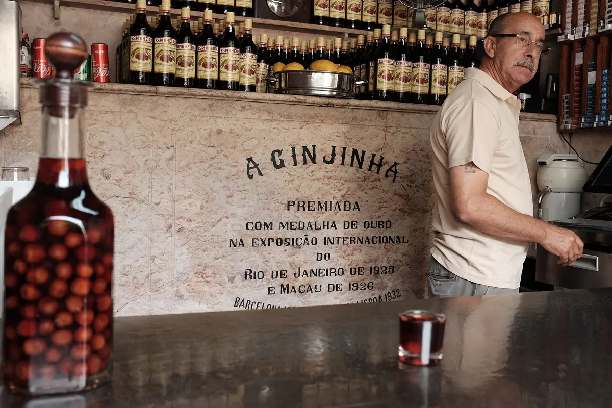A marble counter below a wall lettered A GINJINHA, with rows of Espinheira bottles on the shelf behind and a filled glass on the bar