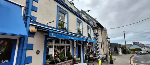 Cream and bright blue pub front with awnings, lanterns and barrels on the pavement, harbour beyond