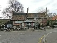 Low flint and brick pub with pantiled roofs and benches outside, the cathedral spire behind