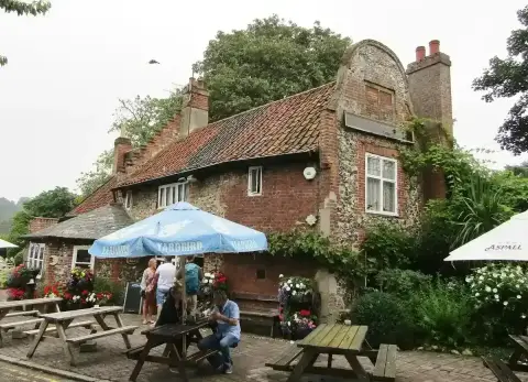 Flint and brick pub with a curved Dutch gable, climbing plants and picnic tables in front