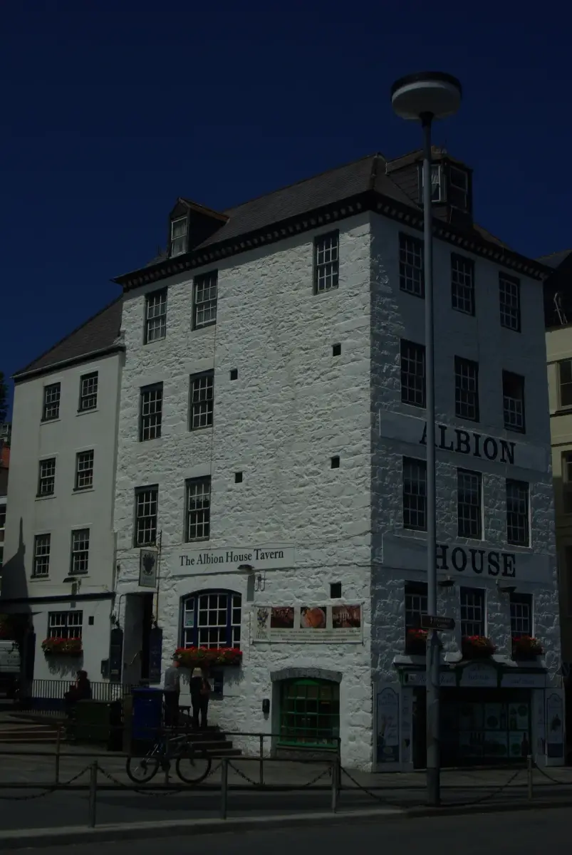 The tall white rubble-stone Albion House Tavern, with ALBION HOUSE painted on its side wall and the tavern's board over an arched window