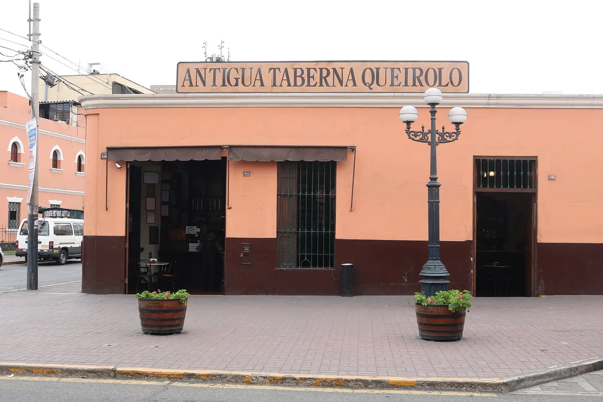 Corner house with Antigua Taberna Queirolo on a long board above, barrels planted at the kerb