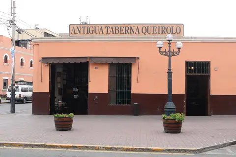 Corner house with Antigua Taberna Queirolo on a long board above, barrels planted at the kerb