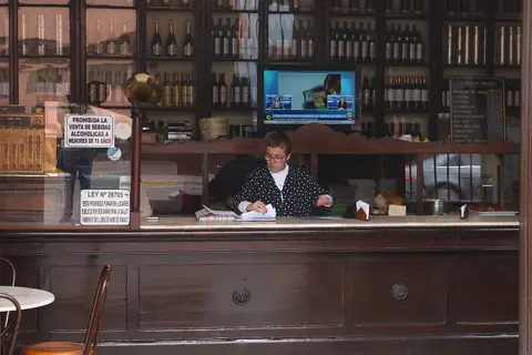 Dark wooden counter and back-bar of glazed cabinets stacked with bottles, a price list chalked up