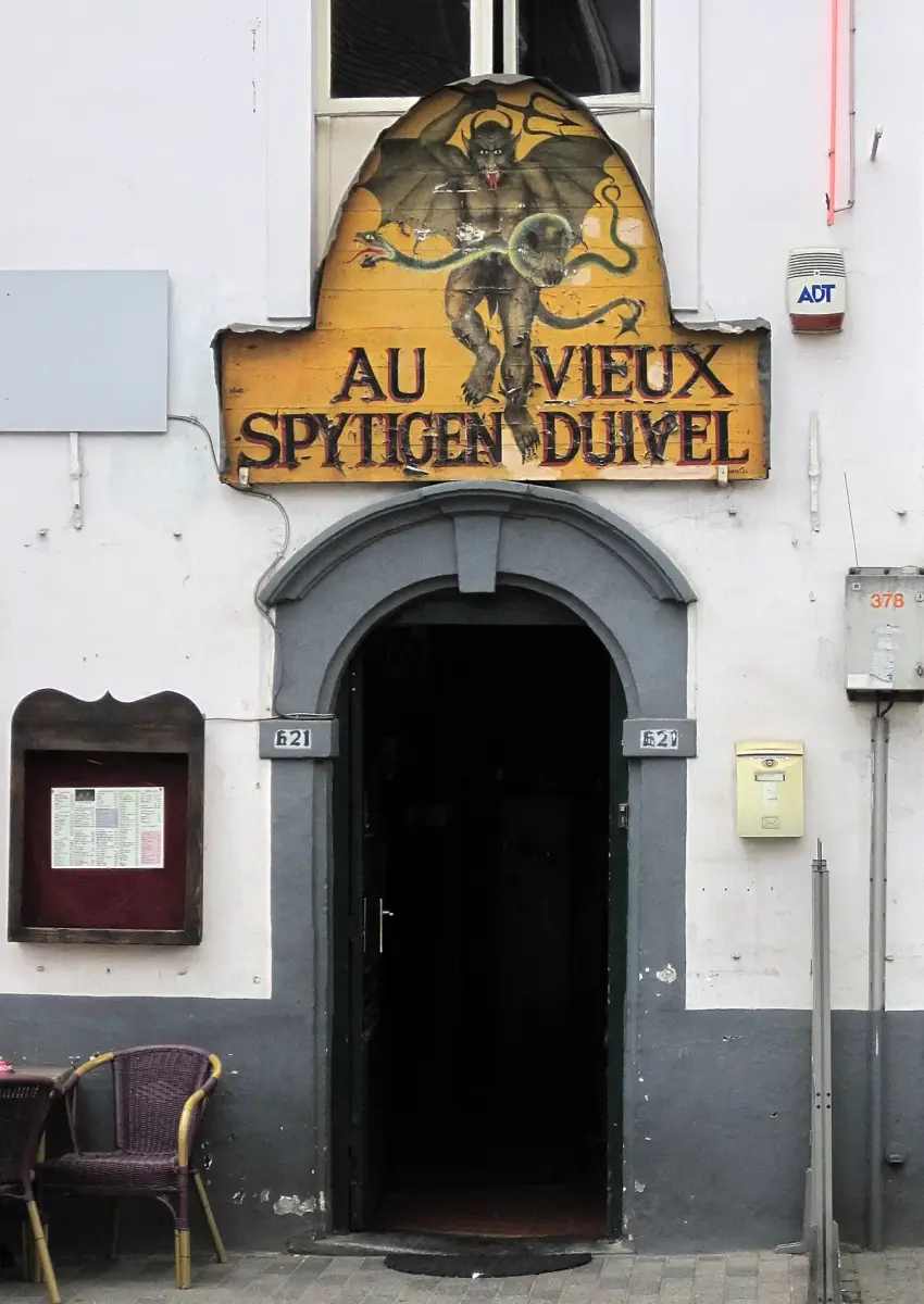 Painted signboard of a red devil over the café doorway, with a menu case and chairs below