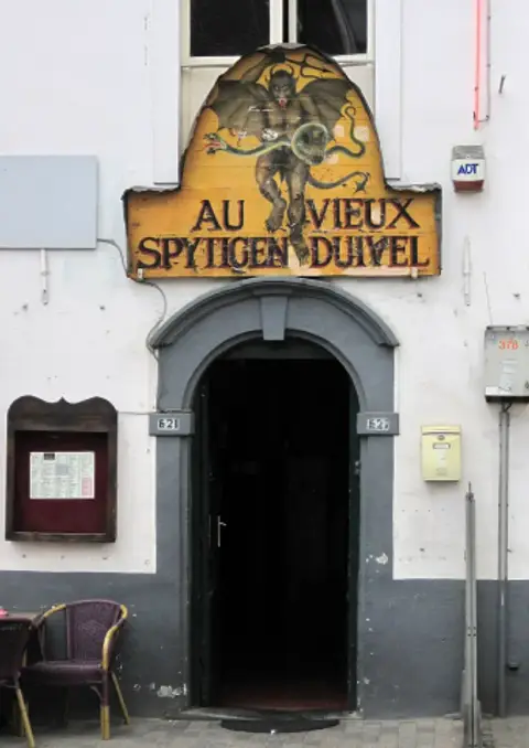 Painted signboard of a red devil over the café doorway, with a menu case and chairs below