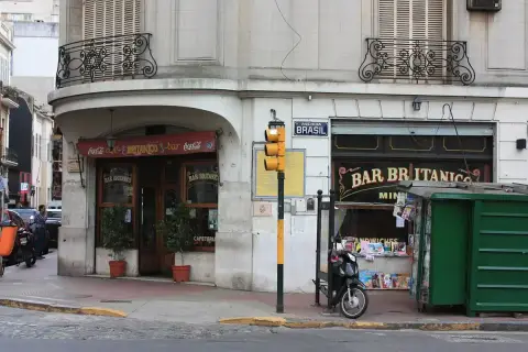 Rounded corner bar with dark timber doors, painted glass lettering and a red awning