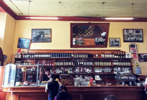 Long mahogany counter below shelves of bottles and framed photographs on a yellow wall
