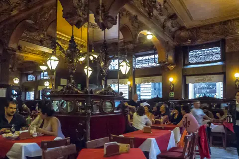 Carved and gilded ceiling over a long room of red-clothed tables, lamps and a mirrored partition