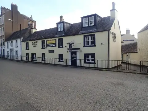 A long cream-washed inn with black window surrounds and dormers, its name in black letters along the front