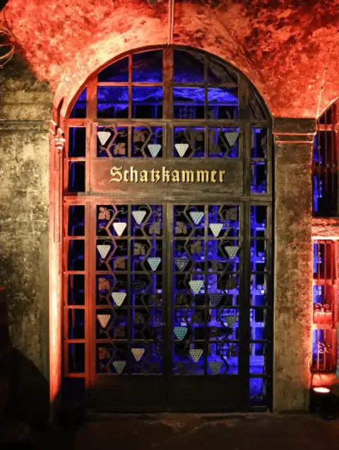 Iron and glass gate lettered Schatzkammer, lit blue and red, with bottles racked behind it