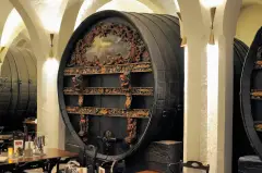 Huge carved and painted wine cask filling an arch of the whitewashed cellar, tables in front of it