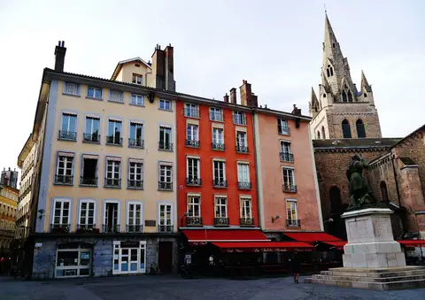 Tall painted houses on place Saint-André, Grenoble, with the red awnings of La Table Ronde along the ground floor and the collegiate church spire at right