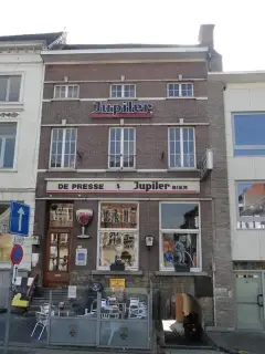 Red-brick front of Markt 50 with DE PRESSE over the café windows, a terrace in front and an arched passage at the side