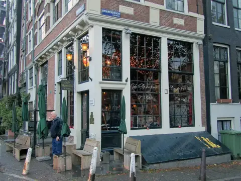 Corner café with small-paned windows and gold lettering reading Café 't Papeneiland, parasols outside