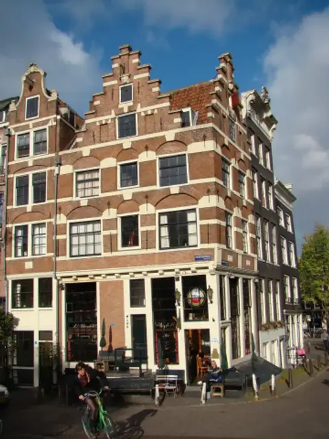 Tall brick canal house with stepped gables on two sides, the café at street level on the corner