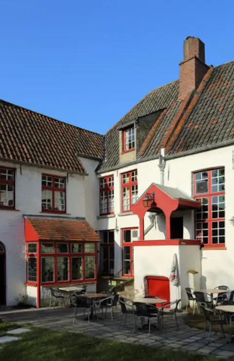 Whitewashed brick buildings with bright red window frames and a red porch around a paved garden