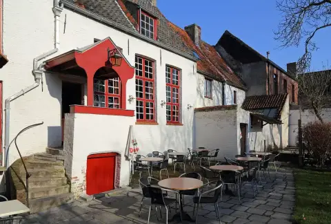 Red-painted porch and cellar door on a whitewashed wall, with cafe tables on the flagstones