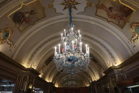 Painted barrel vault with gilt mouldings and a blue Murano glass chandelier over a café counter
