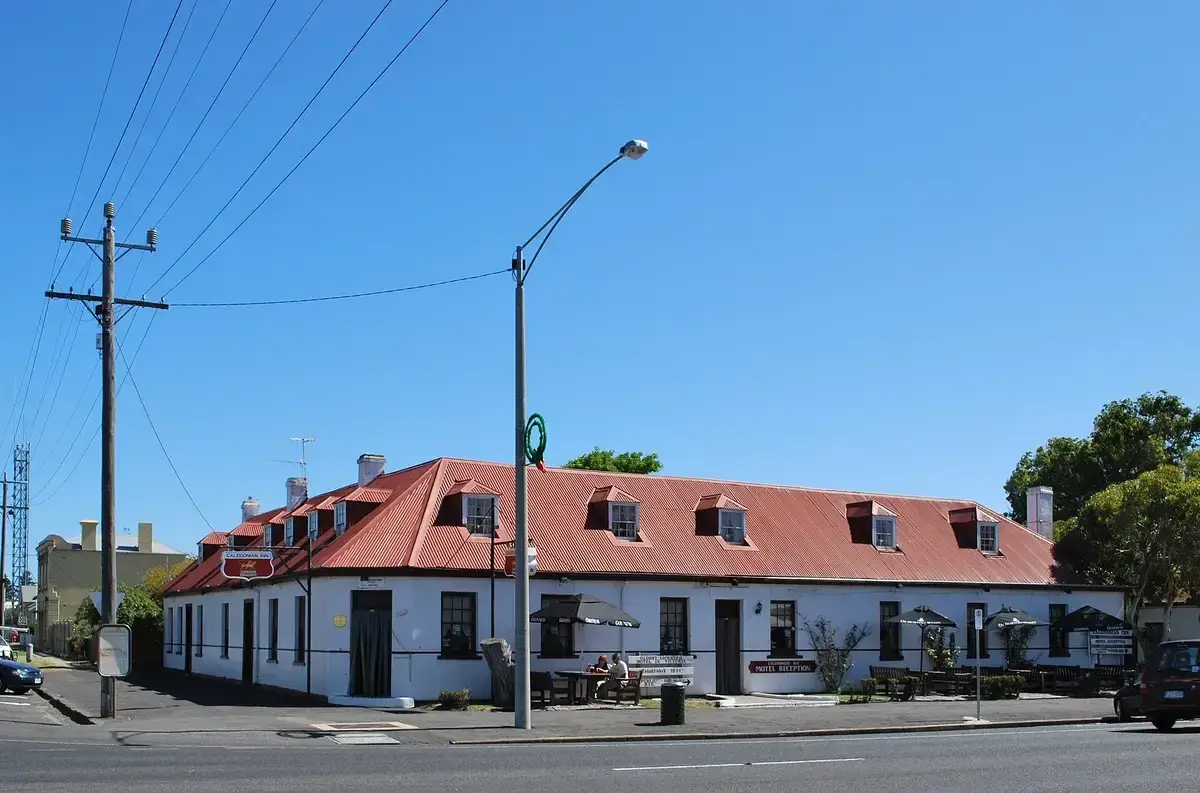Long single-storey white inn with a red corrugated roof and dormer windows on a street corner