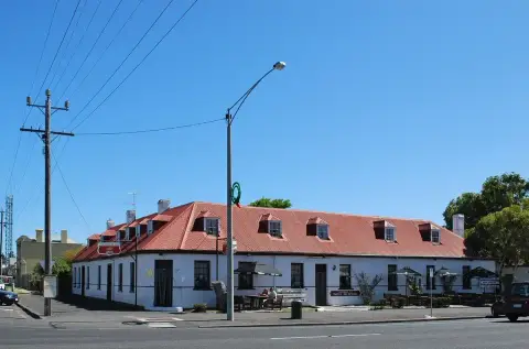 Long single-storey white inn with a red corrugated roof and dormer windows on a street corner