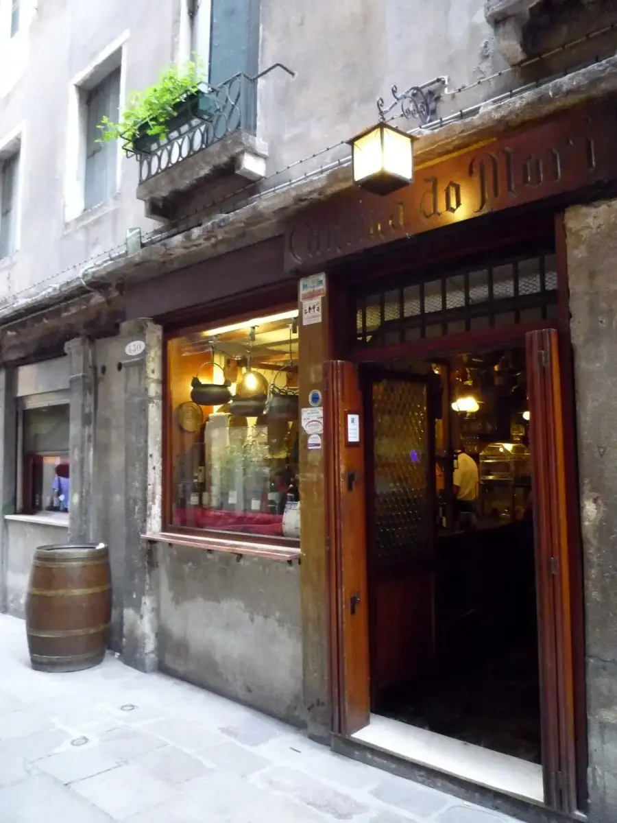Shopfront of Cantina Do Mori in its narrow calle: carved wooden fascia, a lantern over the open door and copper pots in the window