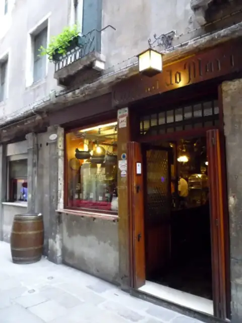 Shopfront of Cantina Do Mori in its narrow calle: carved wooden fascia, a lantern over the open door and copper pots in the window