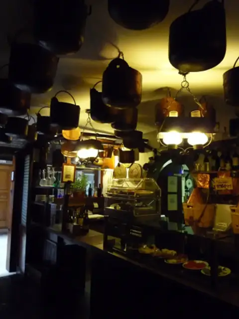 Inside Cantina Do Mori: copper cauldrons hanging from the ceiling over the bar counter and its glass case of cicchetti