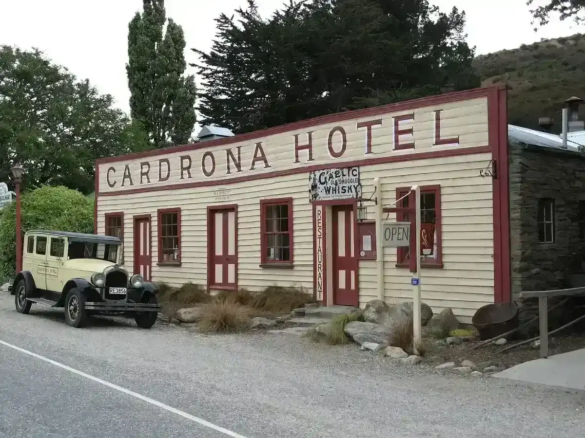 Cream timber hotel with a tall false front lettered in red, a vintage car parked outside