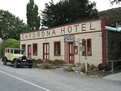 Cream timber hotel with a tall false front lettered in red, a vintage car parked outside