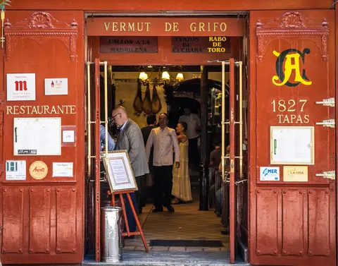 Open doorway lettered Vermut de grifo, hams hanging inside and staff standing in the entrance