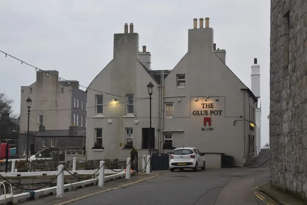 Rendered pub gable on Castletown quay painted The Glue Pot, Est. 1750, castle masonry beyond