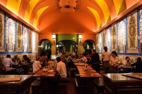 Barrel-vaulted hall with blue and yellow tile panels down both walls and long tables laid in rows