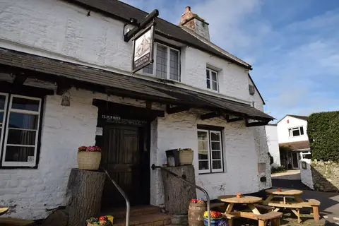 A whitewashed inn with a plank door under a slate porch, the sign reading The Church House Inn and a licensee board beside the door