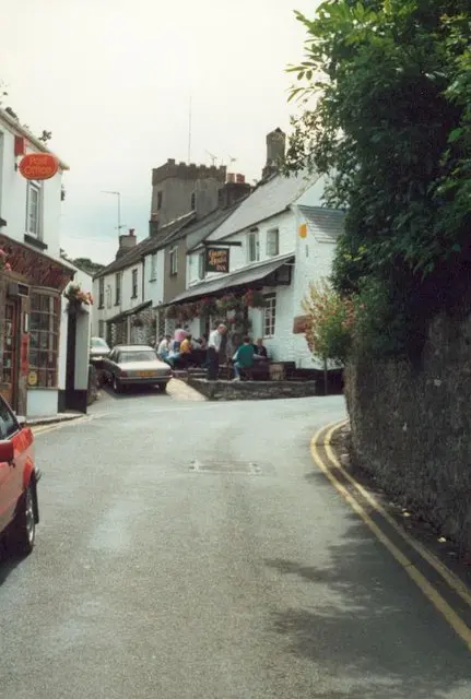 Church Walk at Stoke Gabriel in 1985, drinkers on the inn’s front terrace and the church tower behind