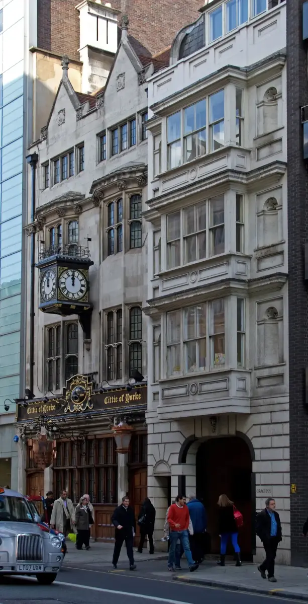 Gabled stone frontage with a projecting clock and gold-lettered fascia, beside the Gray's Inn gate