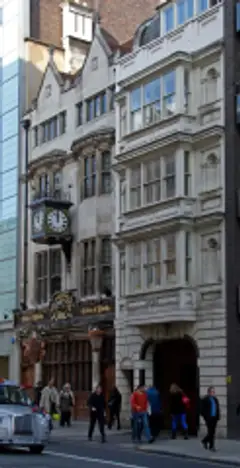 Gabled stone frontage with a projecting clock and gold-lettered fascia, beside the Gray's Inn gate