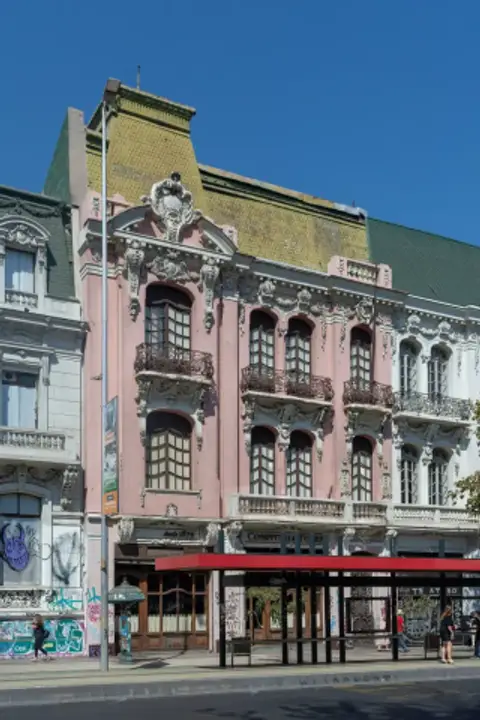 Pink four-storey building with heavy plaster ornament, iron balconies and a green mansard roof