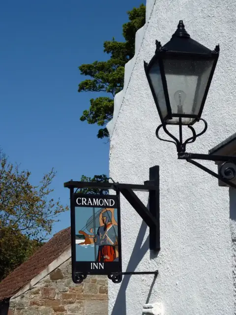 A hanging inn sign painted with a Roman soldier and a boat, lettered Cramond Inn, on a white crowstepped gable beside an iron lamp