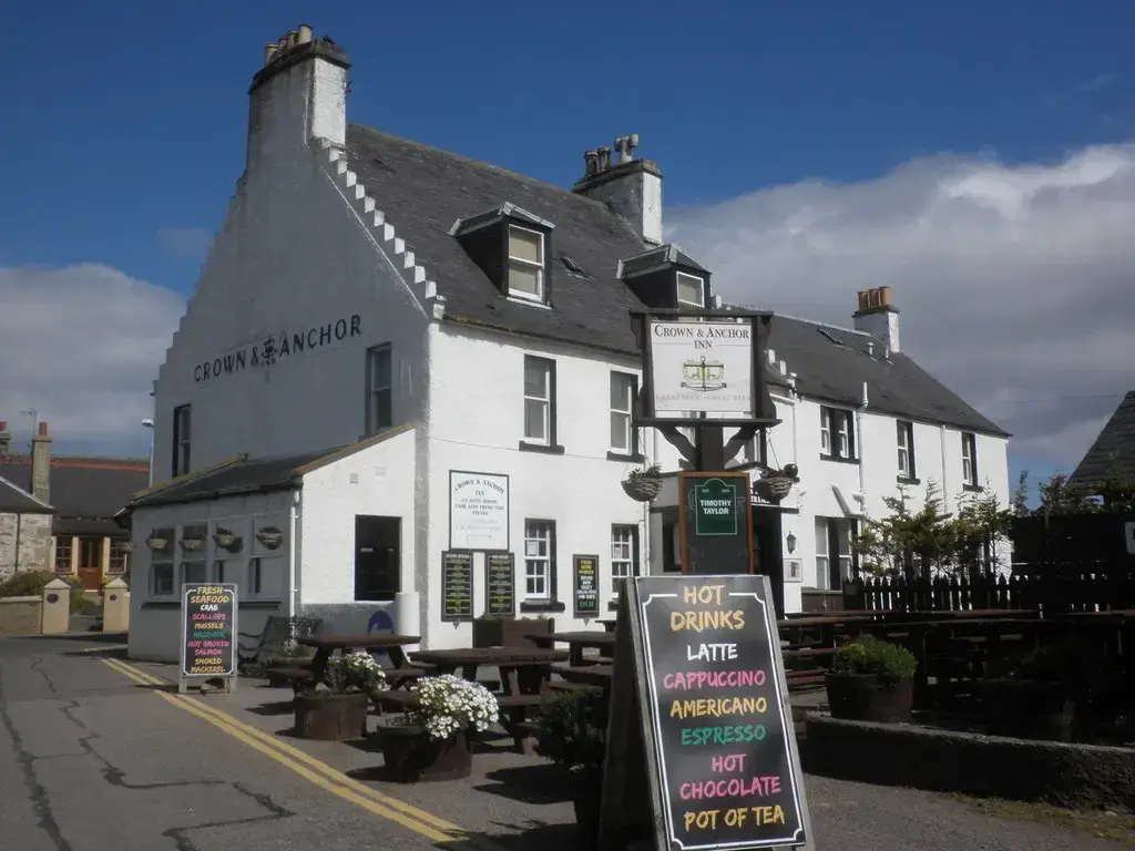 White harled inn with crow-stepped gable and slate roof, its name in black letters on the wall