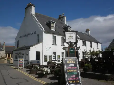 White harled inn with crow-stepped gable and slate roof, its name in black letters on the wall