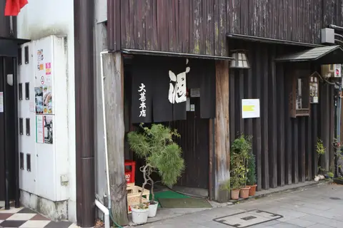 Dark timber shopfront with a black noren reading sake and Daijin Honten, a potted pine beside the door