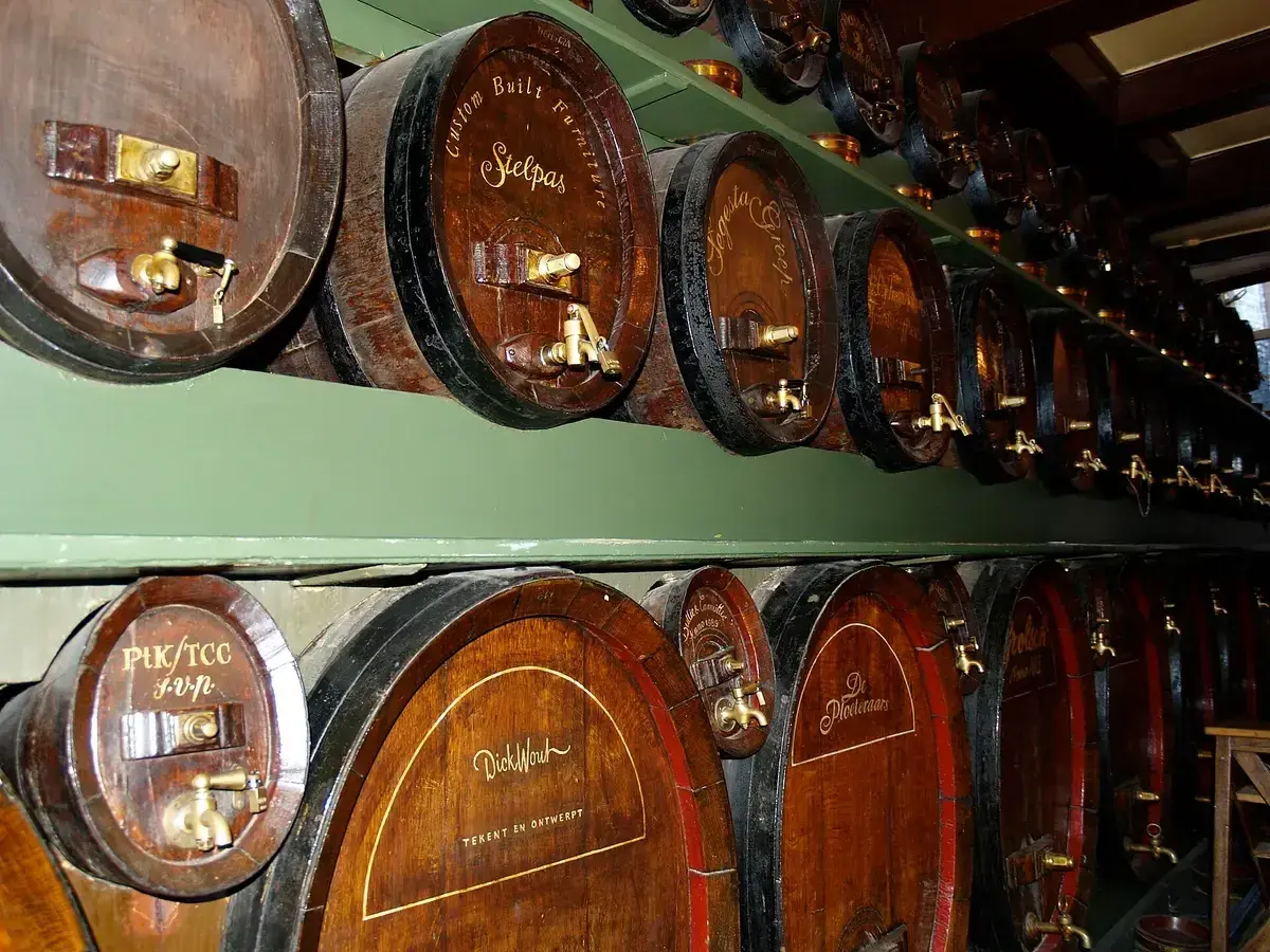 Two tiers of oak casks with brass taps along a green-painted rack, each cask lettered by hand