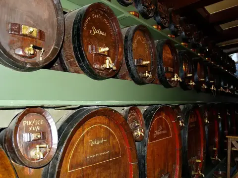 Two tiers of oak casks with brass taps along a green-painted rack, each cask lettered by hand