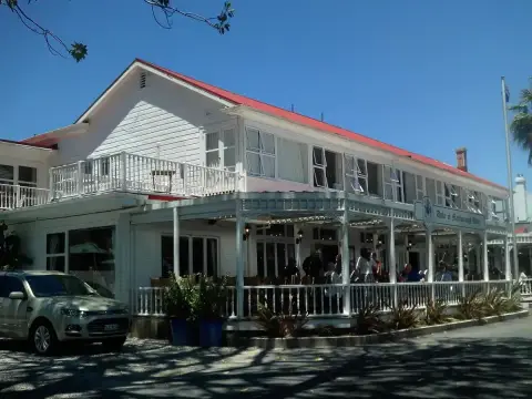 White weatherboard hotel with a red roof and deep two-storey veranda facing the waterfront