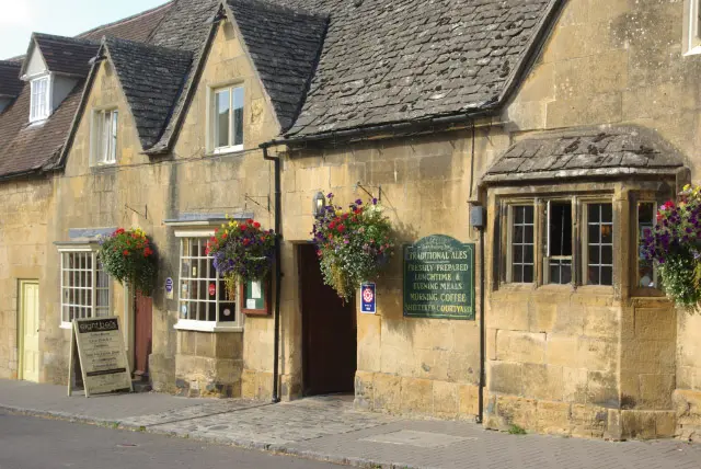 The Cotswold stone front of the Eight Bells with hanging baskets and a painted ales board