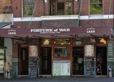 Brick pub front under a deep maroon awning lettered with its name, with open doors to the bar