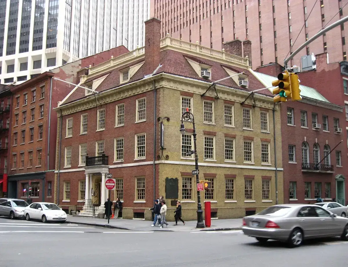 Three-storey red-brick corner building with a hipped roof, dormers and a white porticoed door