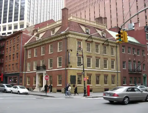 Three-storey red-brick corner building with a hipped roof, dormers and a white porticoed door