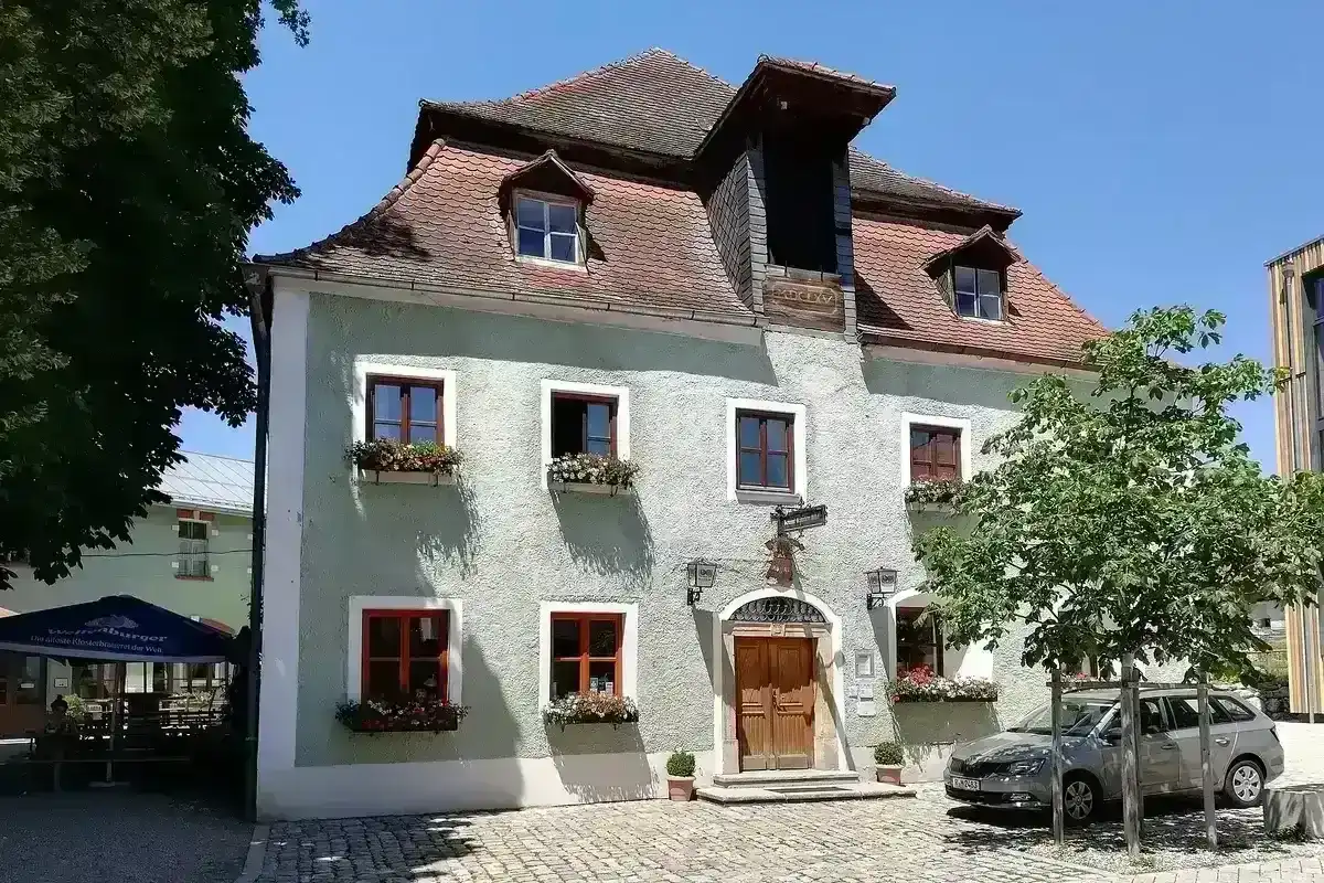Pale green rendered inn with a steep tiled roof, dormers, red-framed windows and flower boxes